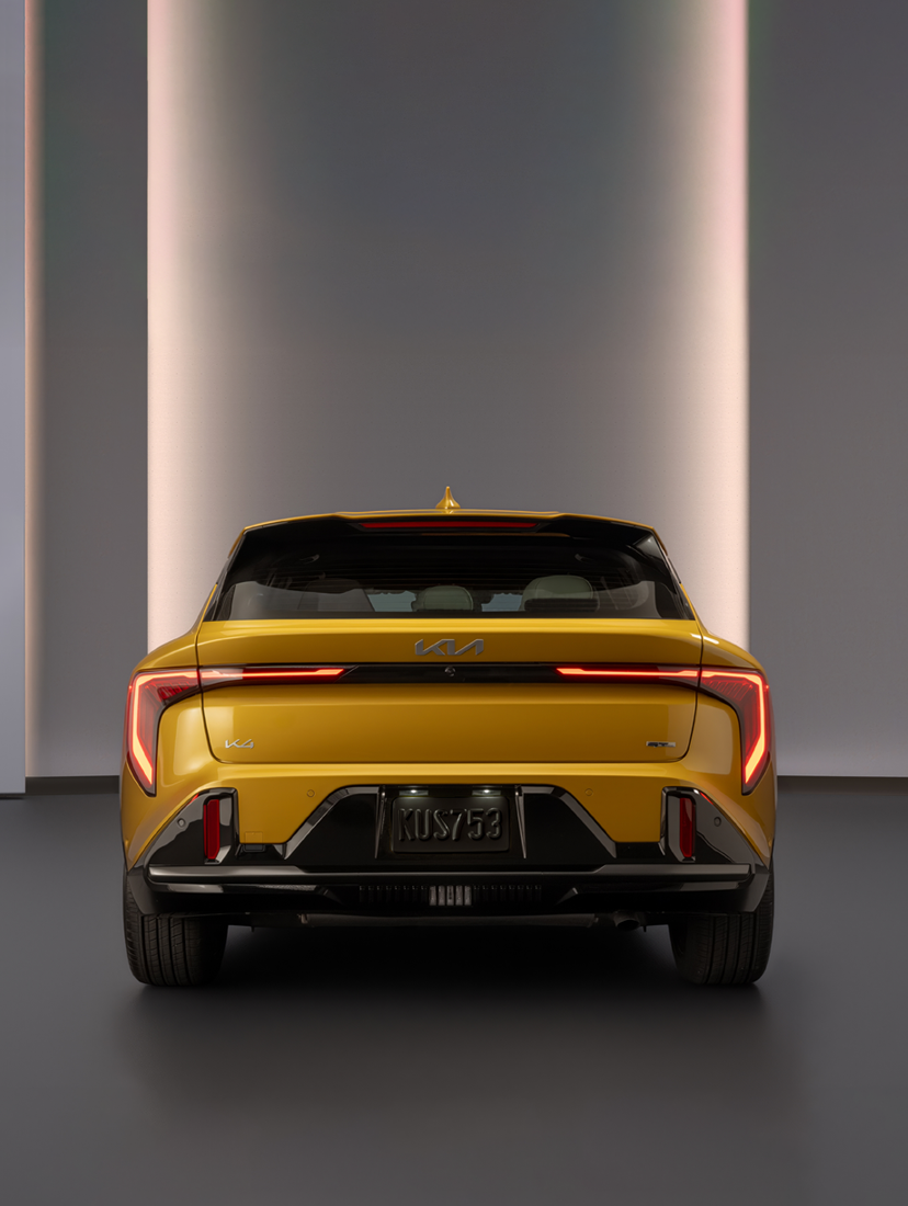 Rear view of a yellow Kia K4 sedan with illuminated LED taillights in a modern studio setting.