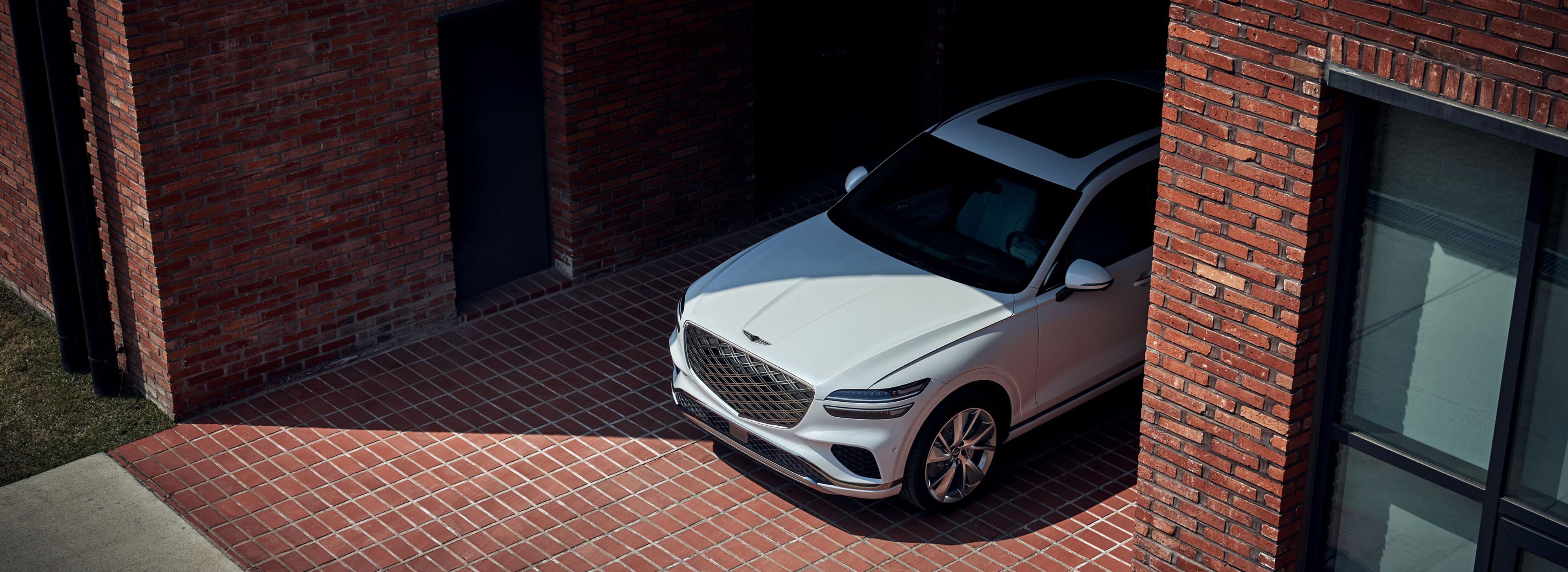 White Genesis GV70 SUV parked in a brick courtyard between two buildings.