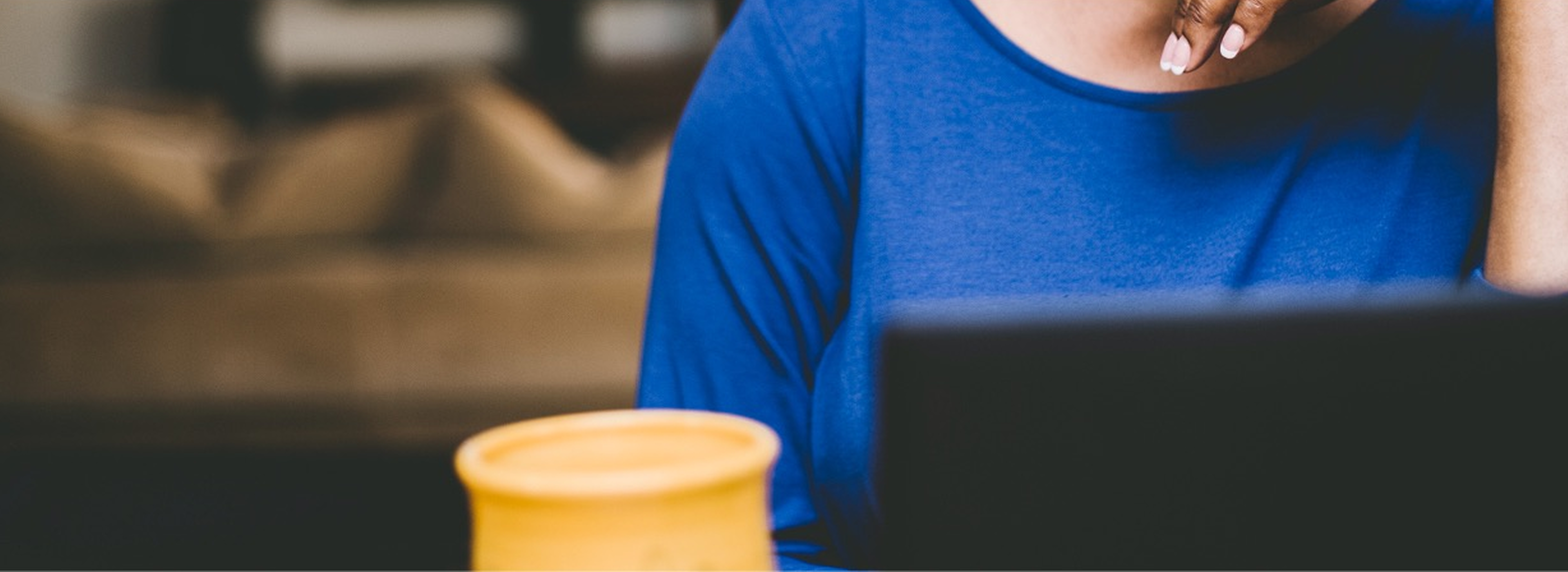 Person using a laptop at a table with a cup nearby.