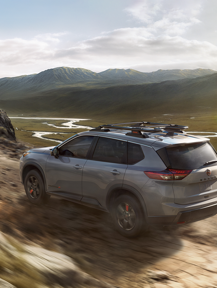 Nissan Rogue driving off-road through rugged mountain terrain, kicking up dust.